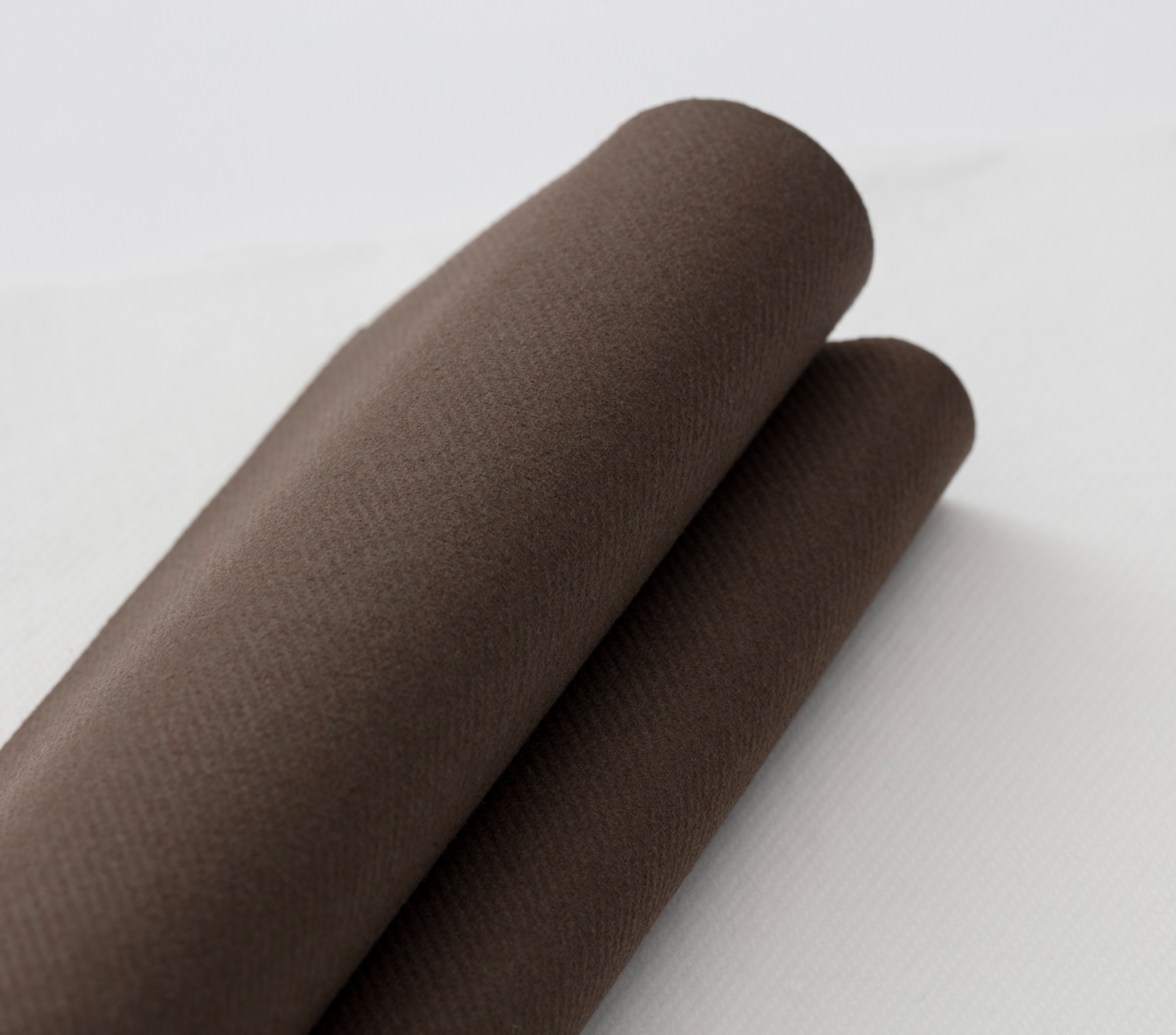 Two brown fabric rolls resting on a white surface, showing a soft suede-like texture.