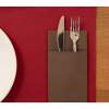 Formal place setting: knife and fork tucked into a brown napkin pocket on a red placemat, with a white plate and wood table edge visible.